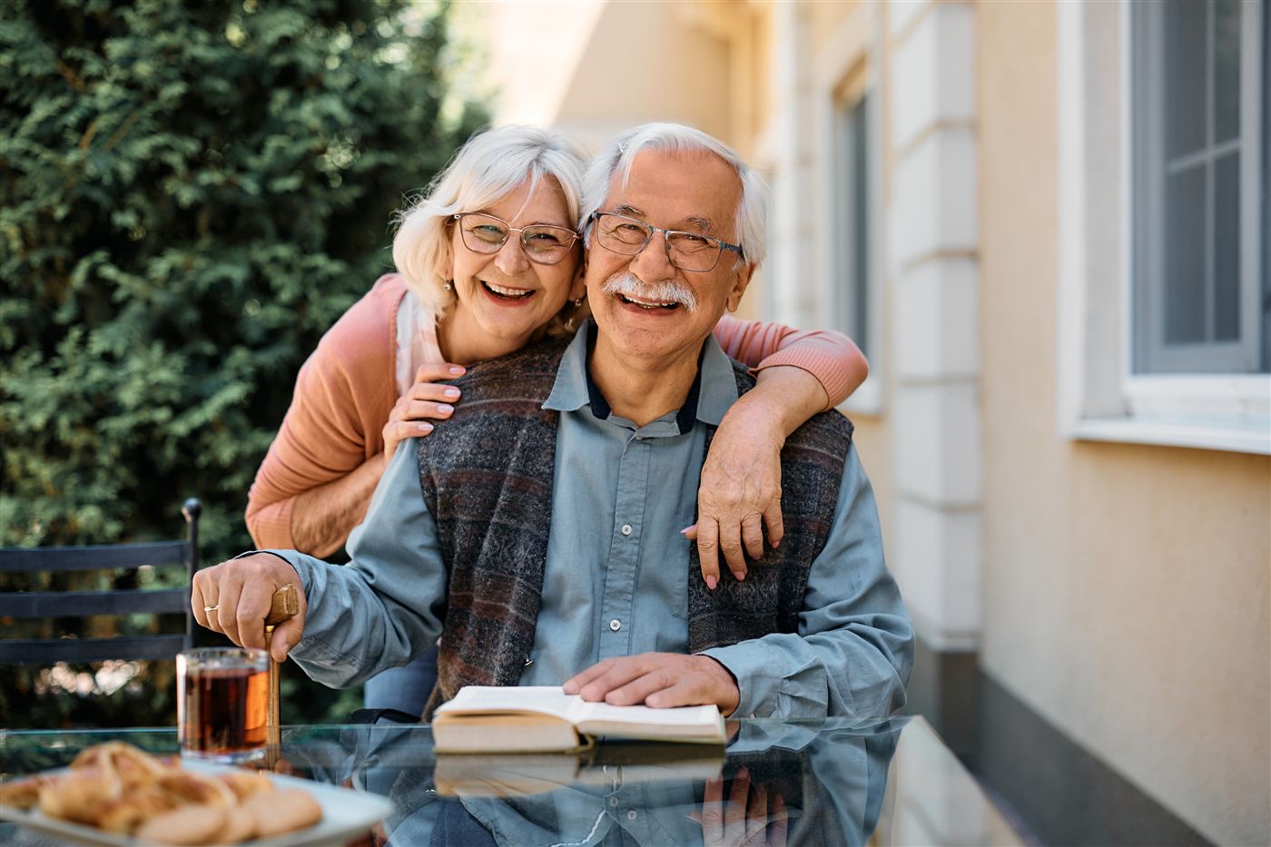 A senior couple smiling and embracing on a sunny porch.
